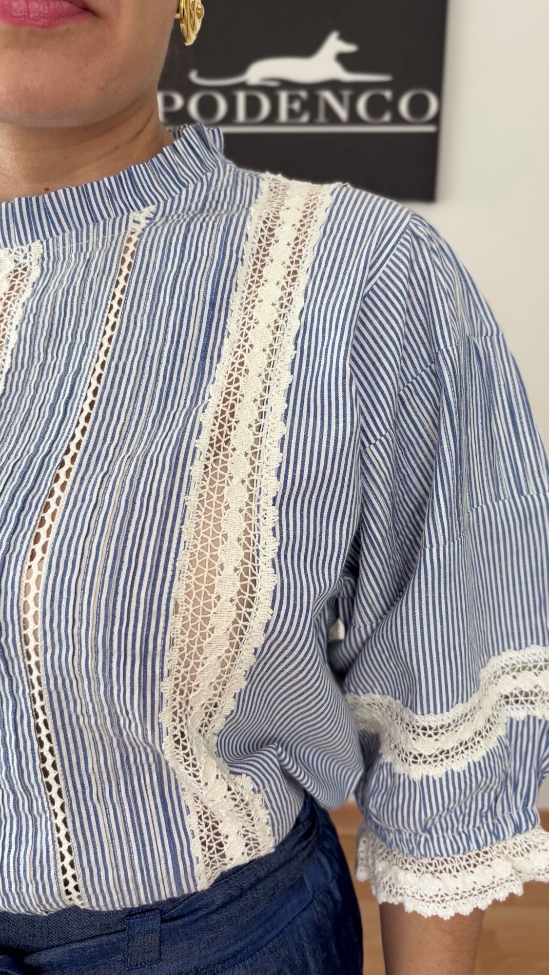 Mujer con la Blusa Ana de rayas verticales azul y blanca, mangas abullonadas y detalle de encaje, posando con estilo relajado y elegante.