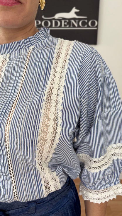 Mujer con la Blusa Ana de rayas verticales azul y blanca, mangas abullonadas y detalle de encaje, posando con estilo relajado y elegante.
