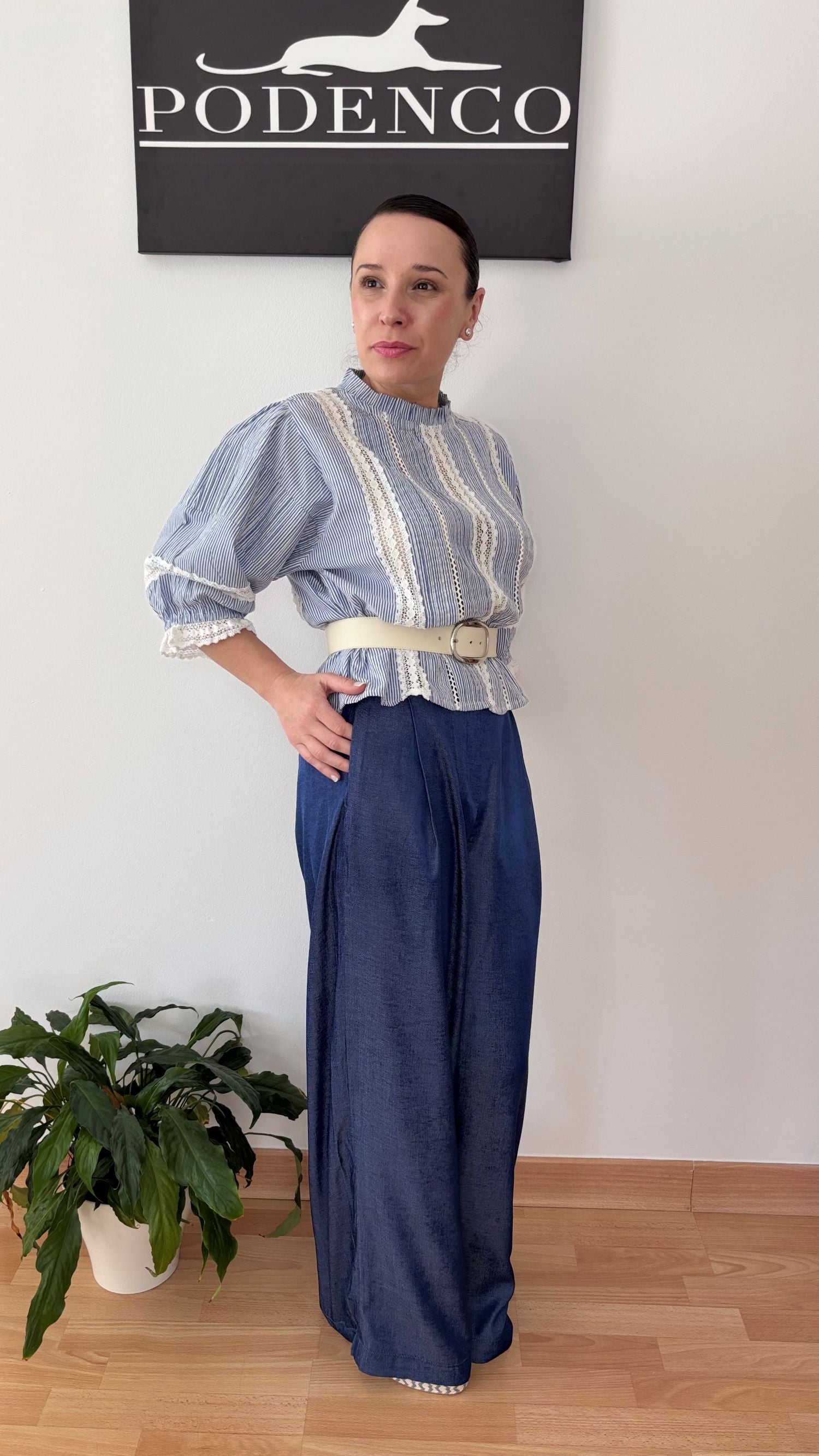 Mujer con la Blusa Ana de rayas verticales azul y blanca, mangas abullonadas y detalle de encaje, posando con estilo relajado y elegante.