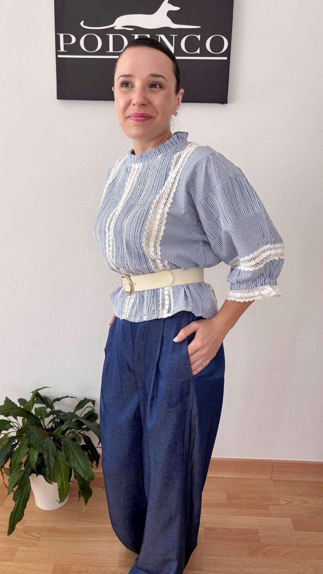 Mujer con la Blusa Ana de rayas verticales azul y blanca, mangas abullonadas y detalle de encaje, posando con estilo relajado y elegante.