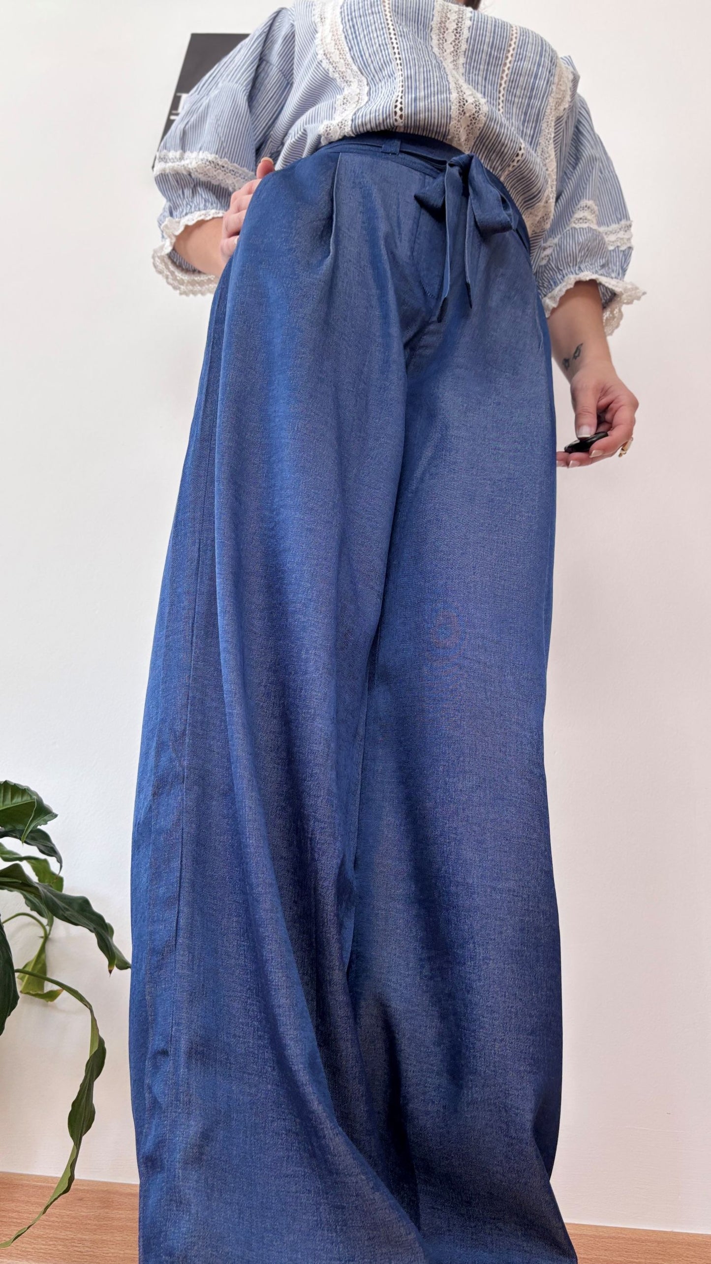 Detalle de una mujer llevando el Pantalón Adara azul de corte palazzo, con cinturilla alta anudada y pinzas, estilizando la figura con caída fluida.