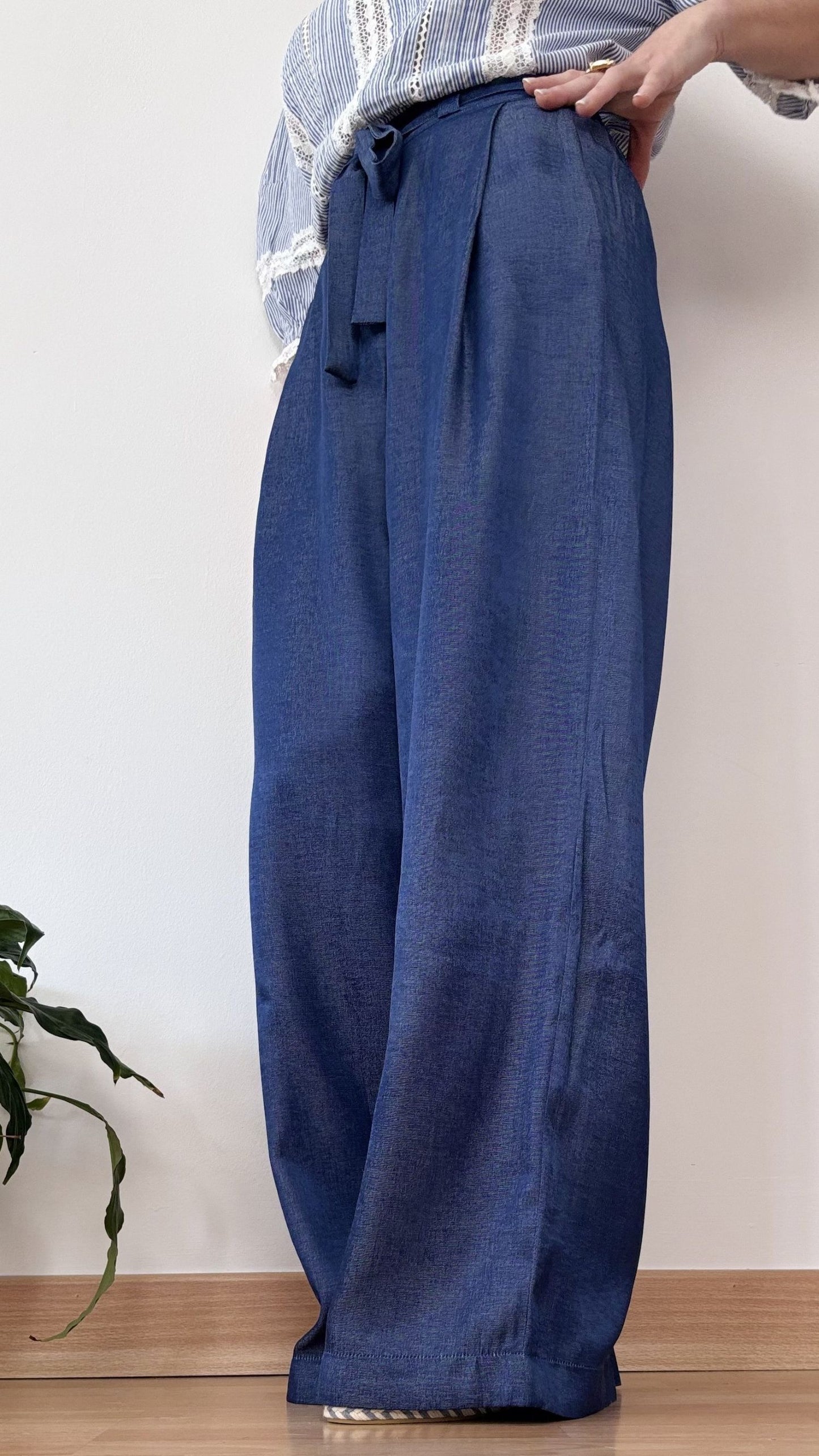 Detalle de una mujer llevando el Pantalón Adara azul de corte palazzo, con cinturilla alta anudada y pinzas, estilizando la figura con caída fluida.